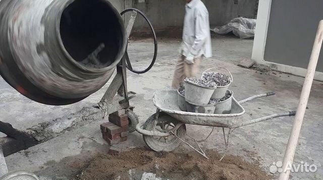 рабочий заливает воду в бетономешалку с сухой смесью